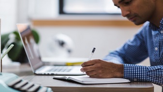 Imagen de una persona trabajando con una libreta y una computadora